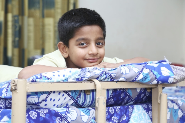 A young orphan boy sat on a bed in Pakistan