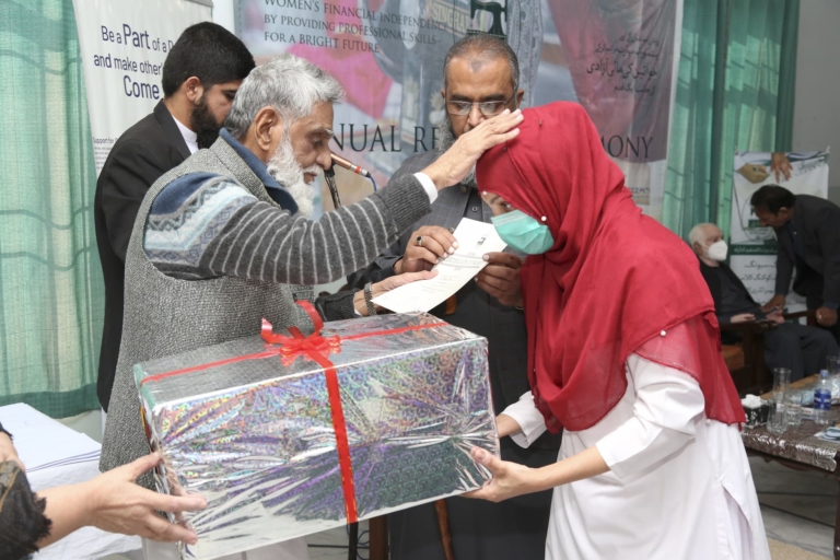A woman receiving a gift from the Al-Zohra Sadiq Vocational Institute