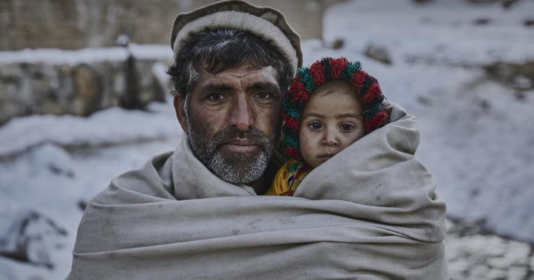 A man and his young child wrapped in a blanket in the cold Pakistan winter