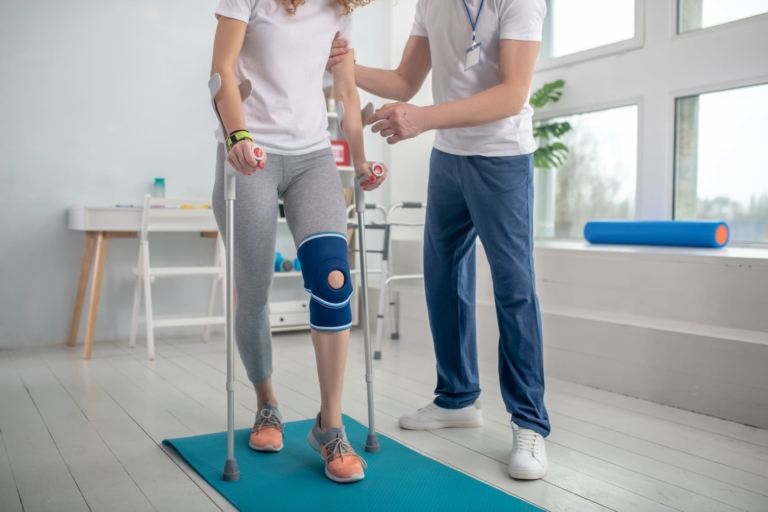 A physiotherapist supporting a patient to walk with crutches