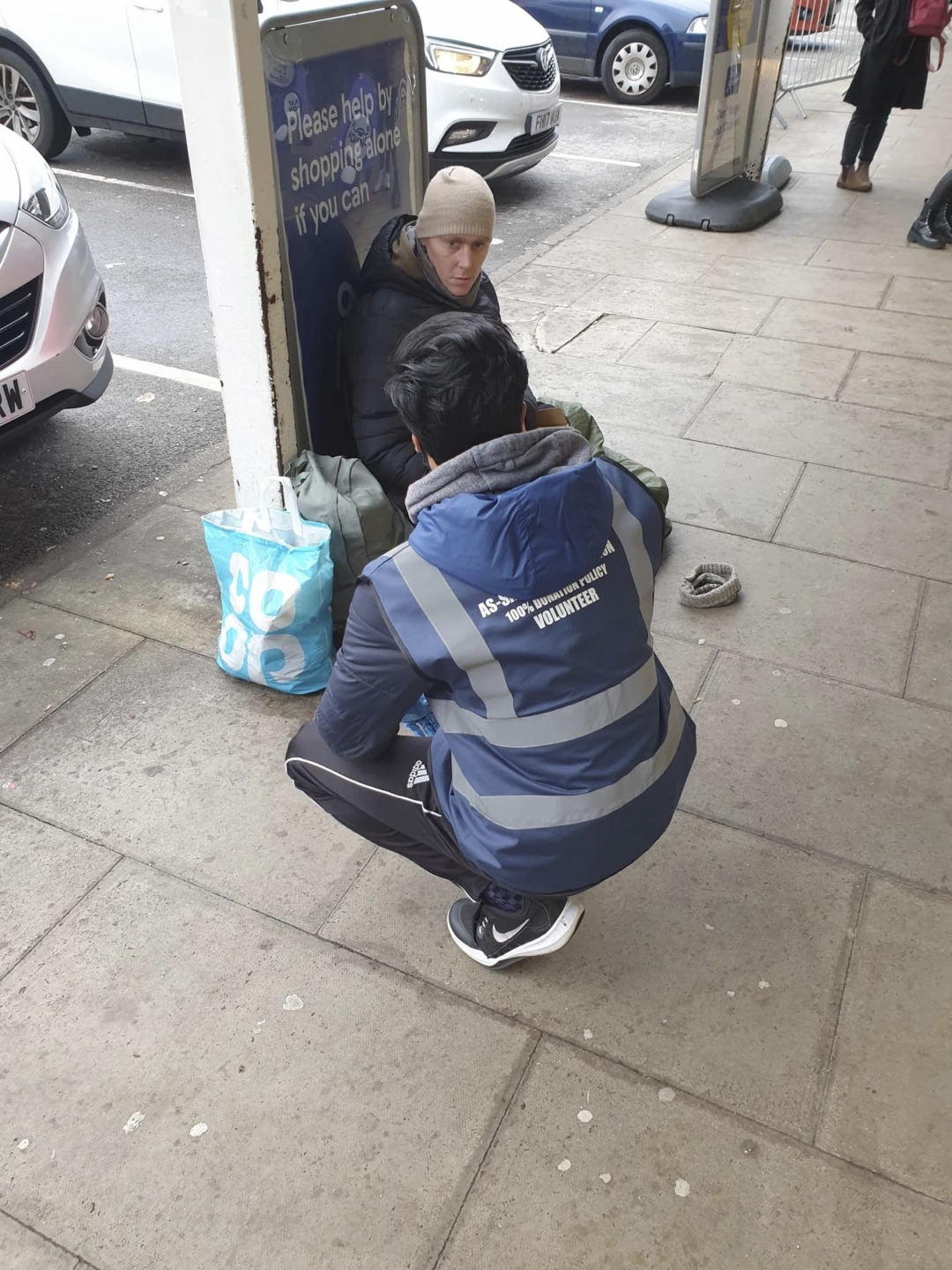 A young volunteer kneeled over helping a homeless man in the UK